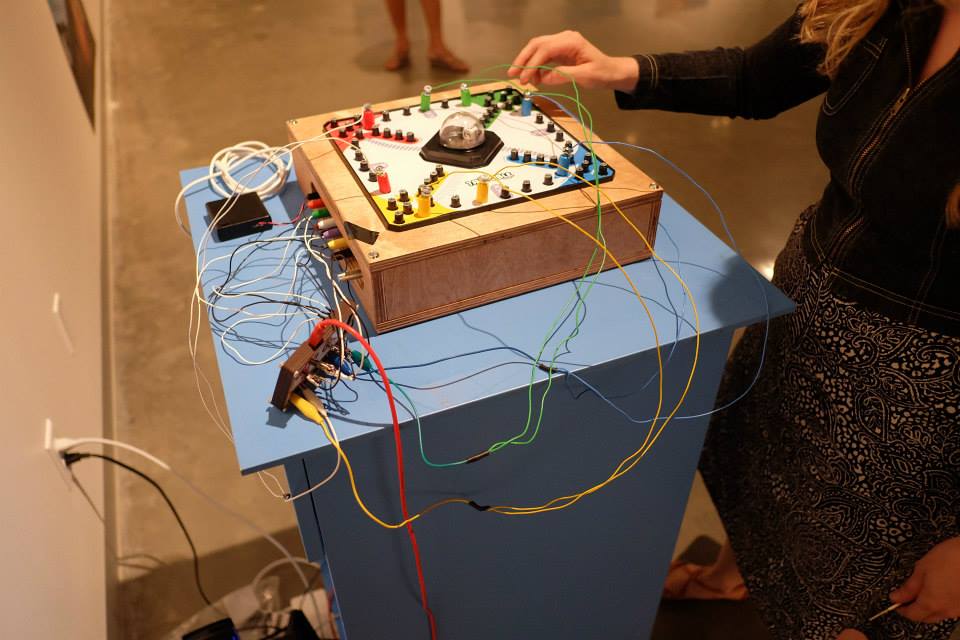 The Trouble Board, a board game prepared with metal contact points for each space along the game path and an embedded microphone under the “pop-o-matic” bubble dice—allow audience members to control a digital soundscape through play. A Makey-Makey microprocessor circuit and a custom-made software patch allow movement around the board and the clicking of the bubble dice to trigger the playback of sound files and process the sound of the dice roll in real-time.